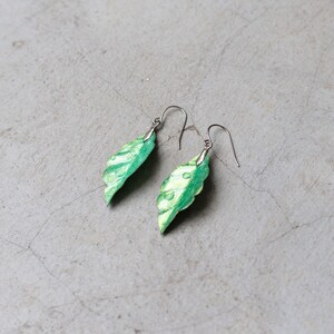 May include: A pair of silver leaf earrings with a green and gold iridescent finish.