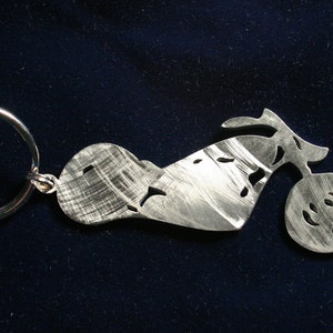 May include: A silver metal motorcycle keychain with a detailed design. The keychain is attached to a silver key ring.