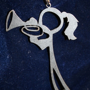May include: Silver-colored metal keychain pendant in the shape of a person playing a trumpet. The pendant is attached to a silver keyring with other keys. The background is a dark blue fabric.