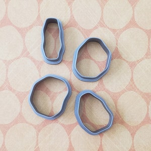 May include: Four gray plastic cookie cutters in different shapes: a rectangle, a rounded rectangle, and two freeform shapes.