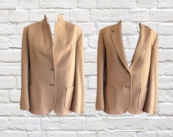 Könnte beinhalten: Zwei beigefarbene Blazer werden vor einer weißen Backsteinmauer präsentiert. Jeder Blazer hat einen Reverskragen, zwei Vordertaschen und Knopfverschlüsse. Die Blazer sind mit einem klassischen Design zugeschnitten, das für verschiedene Anlässe geeignet ist.