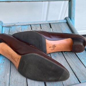 May include: A pair of brown leather heeled shoes with a black rubber sole. The shoes are made in Italy and have a simple, elegant design.