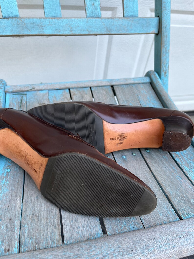 May include: A pair of brown leather heeled shoes with a black rubber sole. The shoes are made in Italy and have a simple, elegant design.
