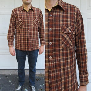 May include: A long-sleeved flannel shirt with a brown and tan plaid pattern. The shirt has two chest pockets and a button-down collar.