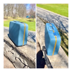 May include: A vintage blue suitcase with yellow, red, and blue stripes. The suitcase is sitting on a stone wall.