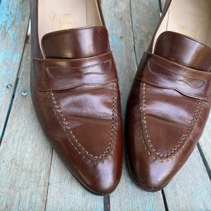 May include: A pair of brown leather loafers with a pointed toe and a stitched design. The loafers have a leather lining and a leather sole.