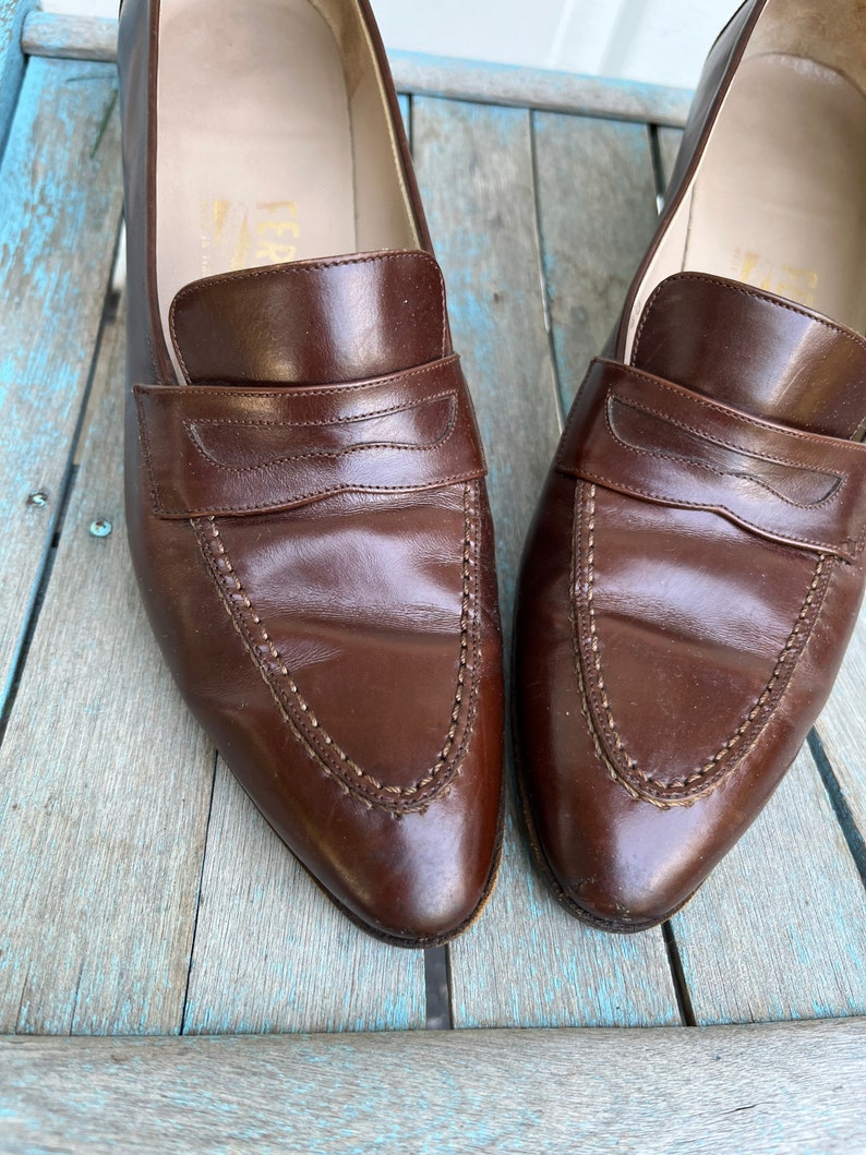 May include: A pair of brown leather loafers with a pointed toe and a stitched design. The loafers have a leather lining and a leather sole.