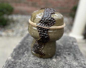 May include: A handcrafted ceramic container with a lid. The container is a muted green colour with a textured, dark brown band around the middle. A light-coloured band encircles the lid. The container is stacked on top of a similar base.