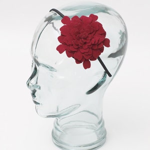 May include: A red felt flower headband. The headband is black and the flower is a large, multi-layered bloom.