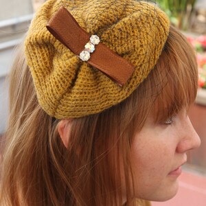 May include: A brown crocheted hat with a brown ribbon and rhinestones. The hat is worn by a person with long, red hair.