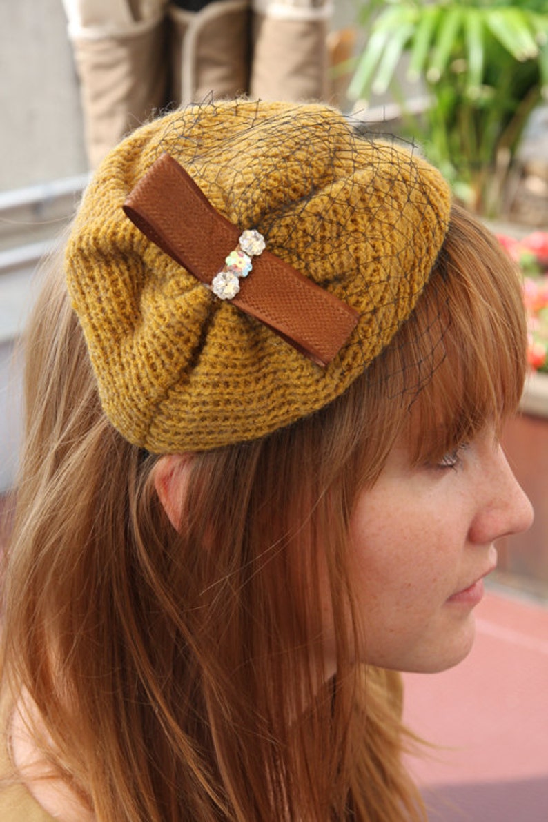 May include: A brown crocheted hat with a brown ribbon and rhinestones. The hat is worn by a person with long, red hair.