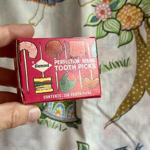 May include: A red box of Diamond Perfection Round Toothpicks. The box has a picture of various foods on toothpicks, including a shrimp, a slice of watermelon, and a hot dog. The box says "Contents: 250 Toothpicks".