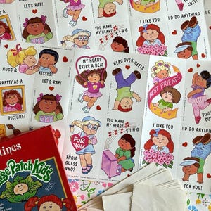 May include: A collection of vintage Cabbage Patch Kids Valentine's Day cards and a red box. The cards feature various illustrations of the dolls with phrases like "Kisses!" and "I like you." The box has the Cabbage Patch Kids logo.