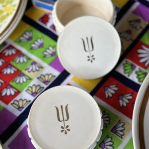 May include: Two white round containers with a gold trident and flower design. The containers are stacked on top of each other.