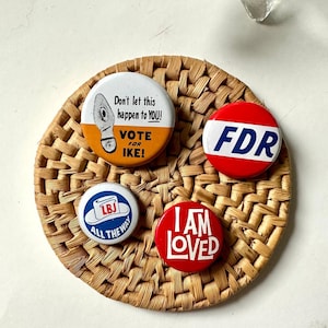 May include: Four vintage political campaign buttons on a woven straw coaster. The buttons feature the text "Don't let this happen to YOU! Vote for Ike!" in orange and white, "FDR" in red and blue, "LBJ All the Way" in blue and white, and "I Am Loved" in white on a red background.