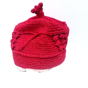 Puede incluir: Un gorro de punto de color rojo con un diseño único que presenta una parte superior puntiaguda y una superficie texturizada.
