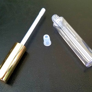 May include: A clear plastic tube with a gold cap and a white applicator. The tube is empty and ready to be filled with lip gloss or other liquids.
