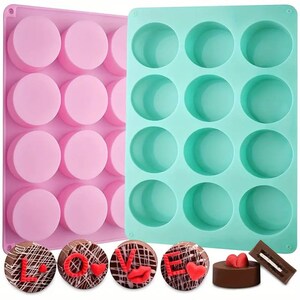 Peut inclure: Deux moules à pâtisserie en silicone, l'un rose et l'autre turquoise, chacun avec 12 cavités rondes. Les moules sont à côté de cinq bonbons au chocolat décorés de cœurs rouges et du mot "LOVE".