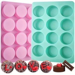 Può includere: Due stampi da forno in silicone, uno rosa e uno turchese, ognuno con 12 cavità rotonde. Gli stampi sono riempiti con caramelle al cioccolato a forma di cuore e la parola "LOVE".