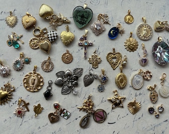May include: A selection of pendants and charms in gold, silver, and jewel tones. The collection includes heart-shaped lockets, crosses, stars, and religious medallions. Some pendants feature intricate details and gemstones.