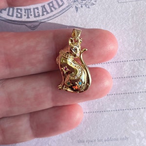 May include: A gold-tone pendant featuring a detailed cat design with colorful gemstones. The cat is sitting with its tail curled around its body.