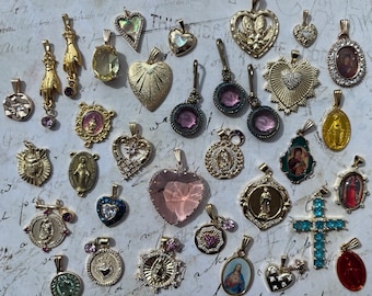 May include: A collection of over 30 silver and gold charms with religious and spiritual themes. The charms feature various designs, including crosses, hearts, and religious figures. Some charms are adorned with colorful gemstones.