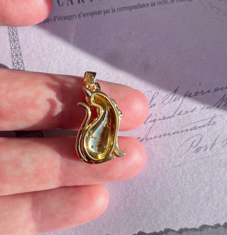 May include: Gold-tone pendant featuring a detailed cat design with red rhinestones. The pendant is shown from the back, revealing the intricate details of the design.