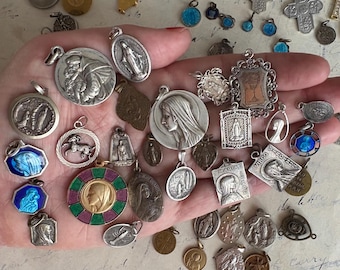 May include: A collection of vintage religious pendants and charms in various shapes and sizes. The pendants are made of silver and gold-toned metals, with detailed religious imagery and enamel accents. Some feature depictions of saints, angels, and religious symbols.