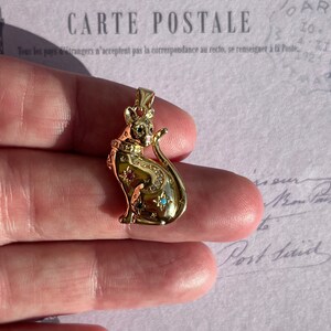 May include: Gold-toned pendant featuring a detailed cat design with a crown on its head. The cat is adorned with small, colorful gemstones.