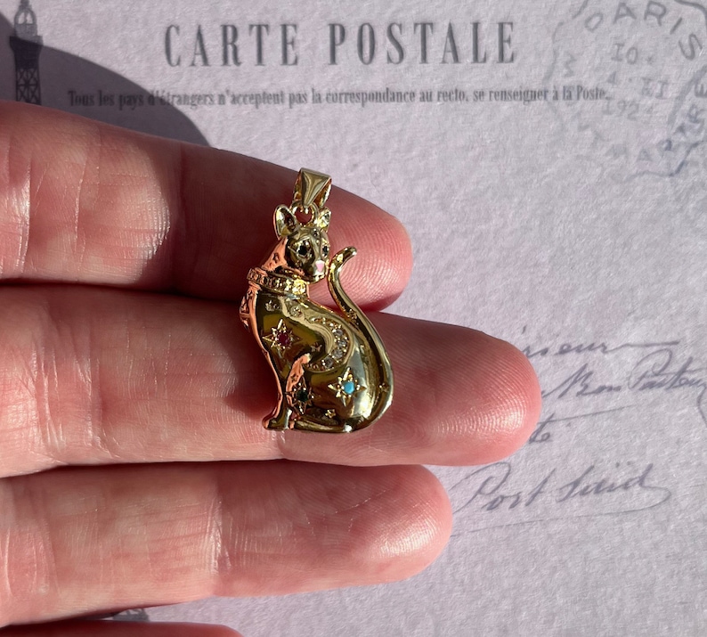 May include: Gold-toned pendant featuring a detailed cat design with a crown on its head. The cat is adorned with small, colorful gemstones.
