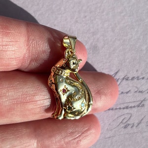 May include: Gold-tone cat pendant necklace with a crescent moon and stars design. The cat is adorned with small, colorful gemstones.