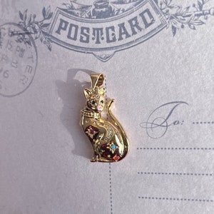 May include: A gold-toned pendant featuring a detailed cat design with colorful gemstones. The cat is sitting with its tail curled around its body.