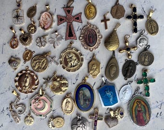 Op de afbeelding: Een verzameling vintage religieuze hangers en bedels, met een verscheidenheid aan stijlen en materialen, waaronder goud, zilver en emaille. De hangers tonen religieuze figuren, symbolen en afbeeldingen.