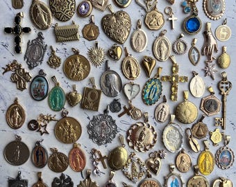 Op de afbeelding: Een verzameling vintage religieuze hangers en bedels, met een verscheidenheid aan stijlen en materialen, waaronder goud, zilver en emaille. De hangers tonen religieuze figuren, symbolen en afbeeldingen.