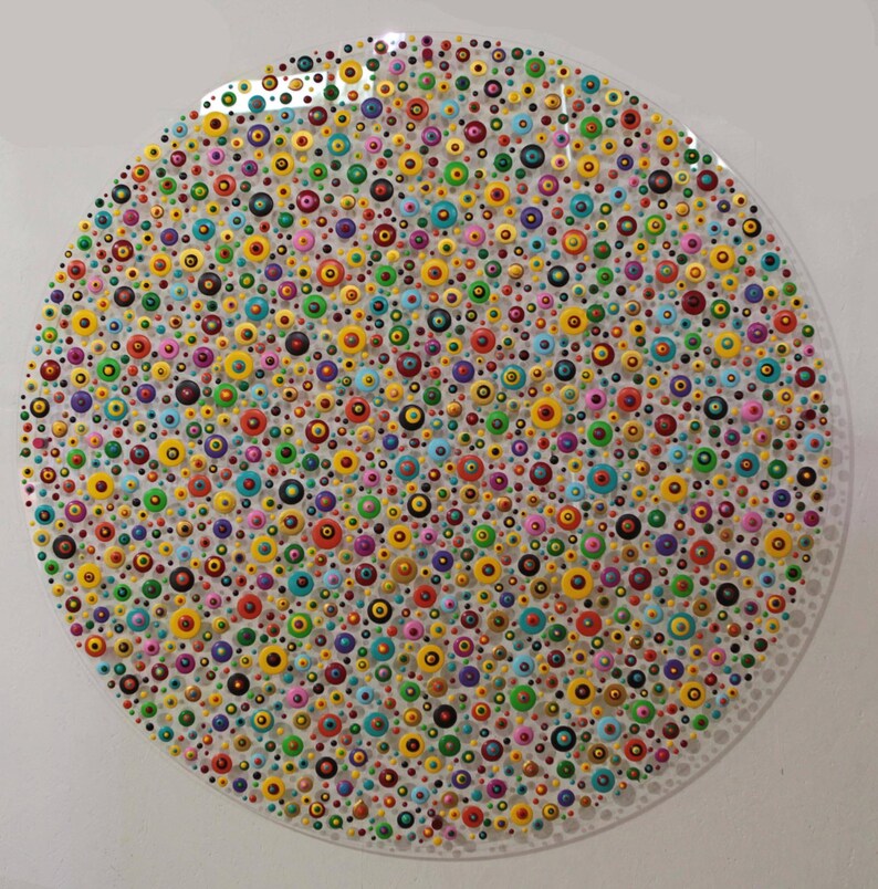 May include: A circular painting with a white background and a pattern of colorful dots. The dots are arranged in a random pattern and are of various sizes. The colors of the dots include red, orange, yellow, green, blue, purple, pink, and black.