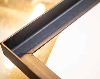 May include: Close-up of a corner of a black and gold picture frame. The frame is made of metal and has a distressed finish.