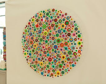 May include: A circular piece of art with a white background and a variety of colorful dots and circles.