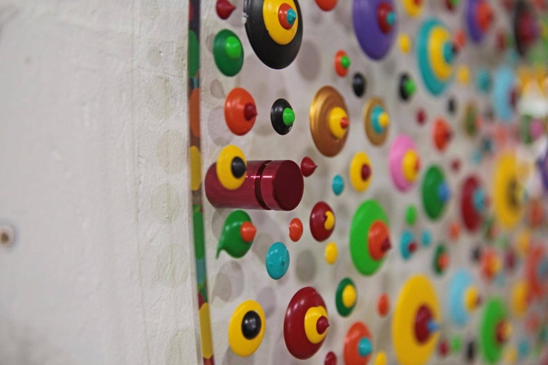 May include: A white wall with a colorful display of round, wooden, painted ornaments. The ornaments are arranged in a pattern and have different colors, including red, green, yellow, blue, and black.