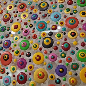 May include: A close-up of a colorful abstract art piece featuring a variety of round shapes with different colors and patterns. The shapes are arranged in a random pattern on a white background.