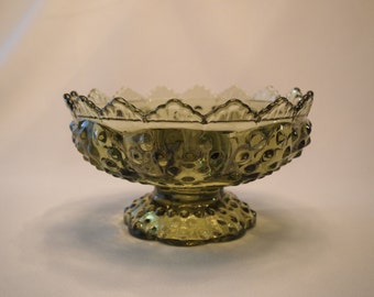 May include: A green glass pedestal bowl with a scalloped rim and a textured, hobnail-like pattern. The bowl sits on a round base and is suitable for serving fruit or displaying decorative items.