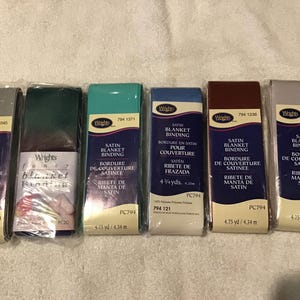 May include: Six packages of Wrights satin blanket binding in various colors including grey, dark green, teal, blue, brown, and silver. Each package is labeled with the brand name, product type, and a length of 4.75 yards, all sealed in clear plastic.
