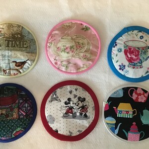 May include: Six round fabric pot holders with different designs.  The designs include teapots, teacups, birds, Mickey Mouse, and a stained glass pattern.  The pot holders have a white, cream, pink, red, blue, or black background.