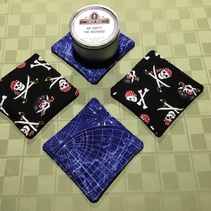 May include: Four square fabric coasters with a pirate skull and crossbones design on a black background and a blue and white world map design. The coasters are on a green checkered tablecloth with a silver tin can in the center.