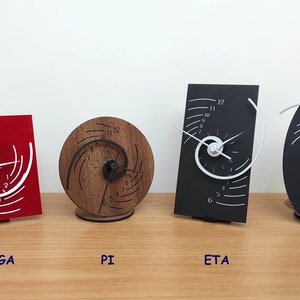 Op de afbeelding: Vier verschillende stijlen van spiraalvormige klokken, elk met een uniek ontwerp. De klokken zijn gelabeld "OMEGA", "PI", "ETA" en "THETA". De klokken zijn 10 cm breed en 14 cm hoog.
