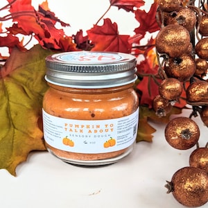 May include: A glass jar of orange pumpkin spice sensory dough with a white label that reads "Pumpkin to Talk About Sensory Dough". The jar is surrounded by fall-colored leaves and decorative orange berries.