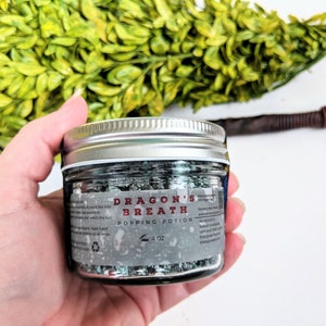 May include: A glass jar with a silver lid filled with a popping potion called "Dragon's Breath" in a gray and green color scheme. The label reads "Popping Potion" and "4 oz".