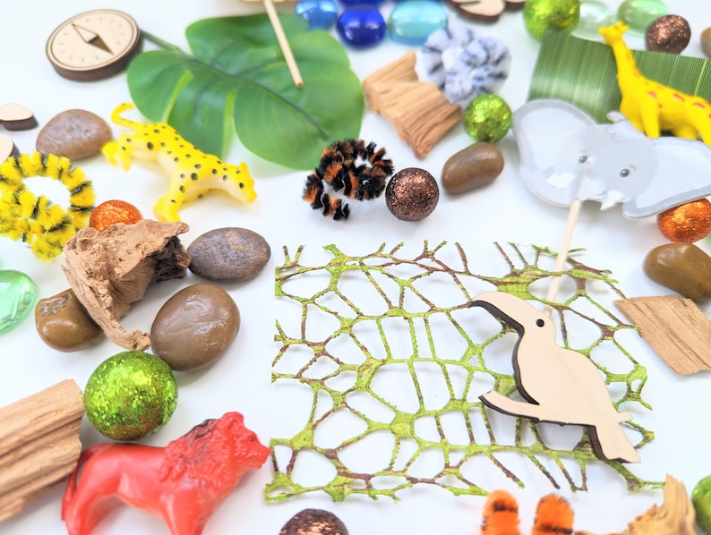 May include: A collection of jungle-themed toys and objects, including a yellow leopard, a brown toucan, a green leafy plant, a brown wooden log, a compass, a grey elephant, a yellow giraffe, a brown wooden stick, a green net, and brown and orange rocks.