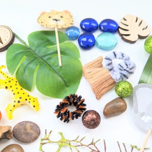 May include: A collection of jungle-themed toys and decorations, including a leopard figurine, a wooden elephant, a green leaf, a compass, and blue and green glass gems.