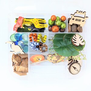 May include: A clear plastic storage box filled with various jungle-themed toys and craft supplies. The box includes a wooden jeep, a toucan, a compass, a tiger, a giraffe, a monkey, leaves, and colorful glass gems.