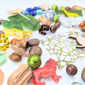 May include: A collection of jungle-themed toys and objects, including a lion, a cheetah, a toucan, a green leaf, a wooden log, a net, and a variety of colorful beads and stones.